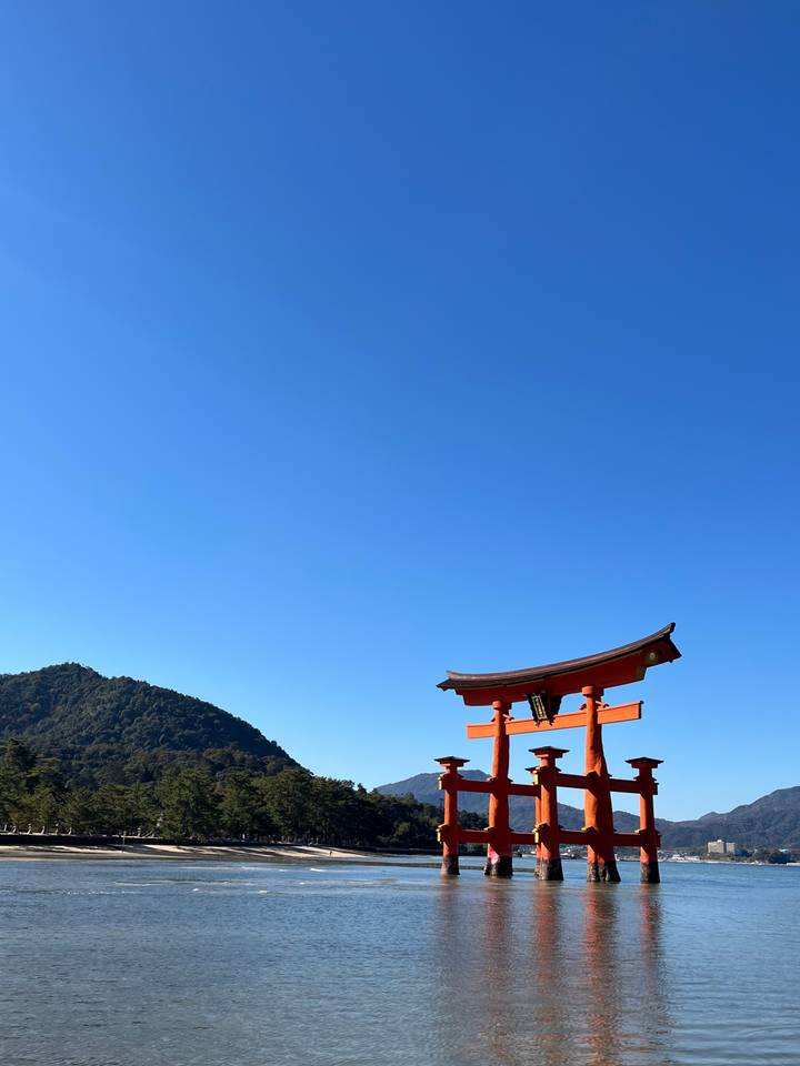 Portique torii contre un ciel bleu dégagé avec des collines au loin.