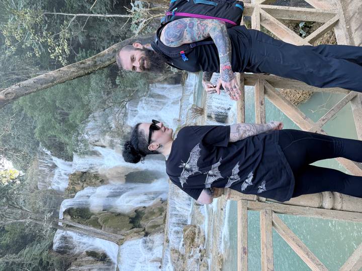 Deux touristes souriants devant une grande cascade.
