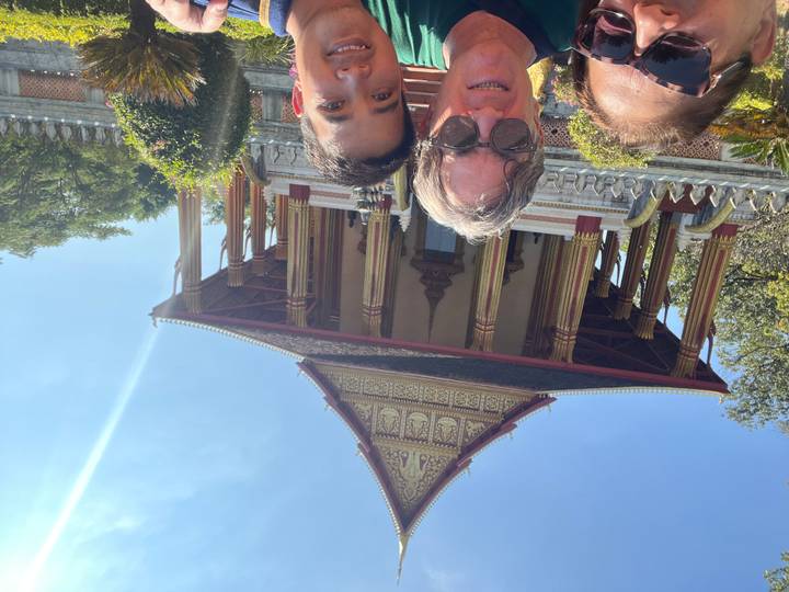 Drie mensen poseren voor een tempel met sierlijke architectuur en blauwe lucht.