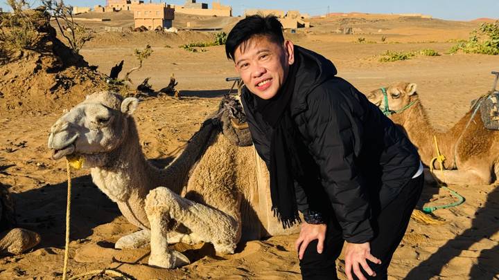 Una persona posa con un camello en un entorno desértico.