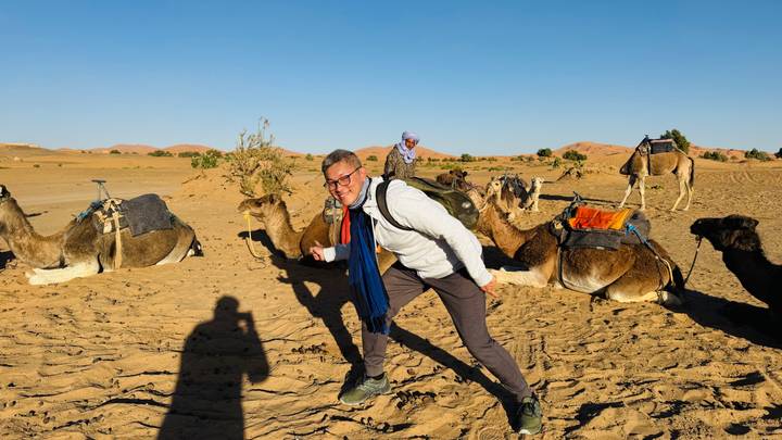 Una persona con camellos y sombras en terreno desértico.
