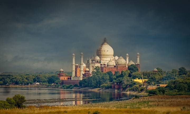 Vue lointaine du Taj Mahal entouré de verdure et d'une rivière.