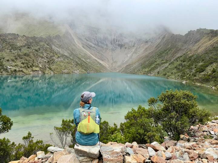 Hiker admiring a serene blue mountain lake surrounded by peaks.
