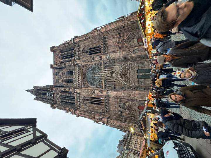 Een grote gotische kathedraal met ingewikkelde details en een menigte mensen ervoor, mogelijk een kerstmarkt.