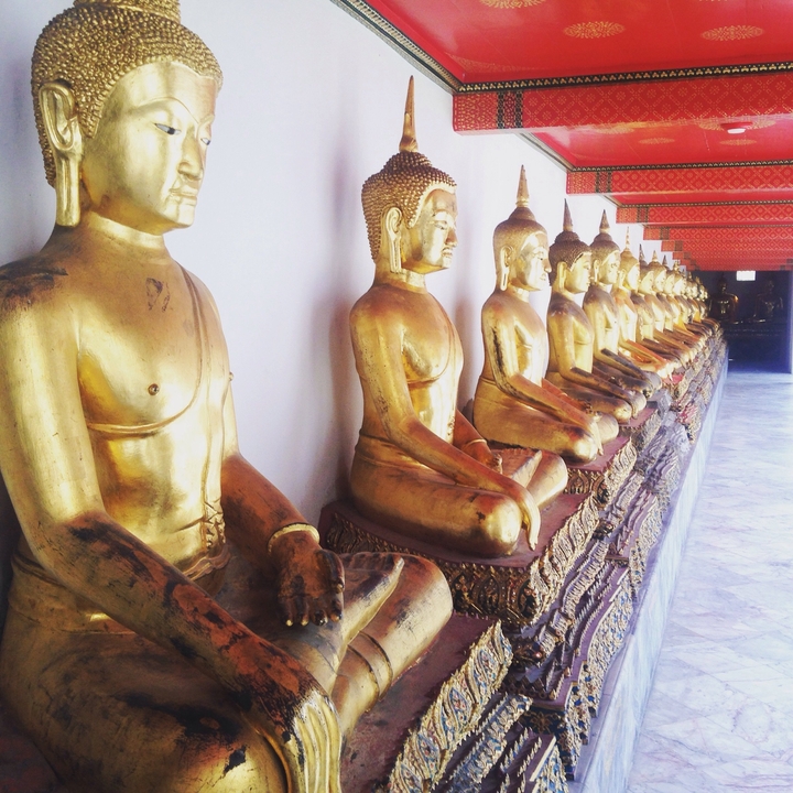 Long row of golden seated Buddha statues inside a Thai temple corridor.