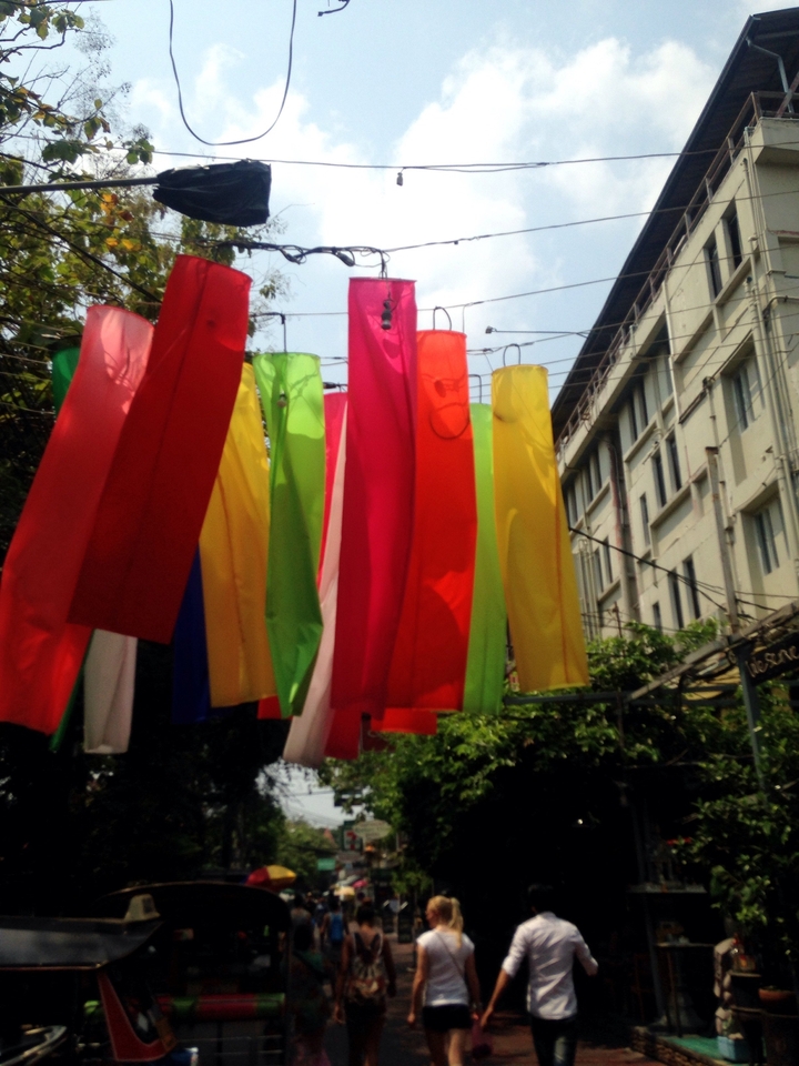 Colorful vertical fabric banners hanging in an outdoor alley beside a white building.