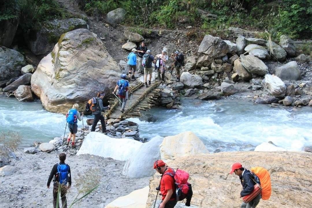 Randonneurs traversant une rivière sur un pont de bois improvisé.