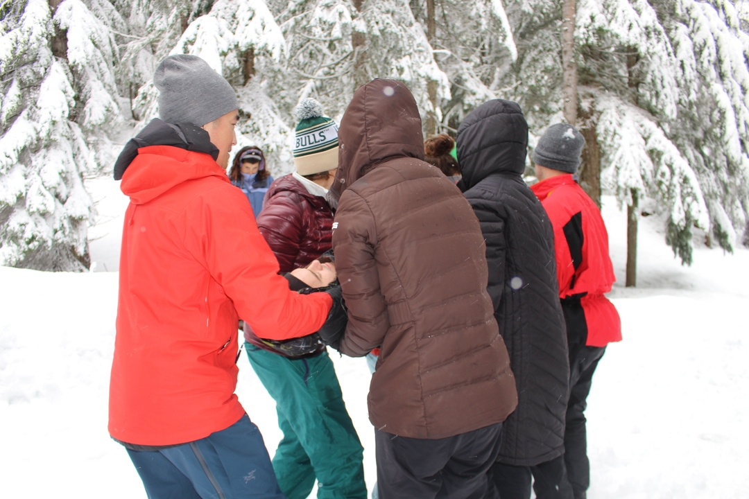 Des personnes vêtues de vestes d'hiver se tiennent dans la forêt enneigée.