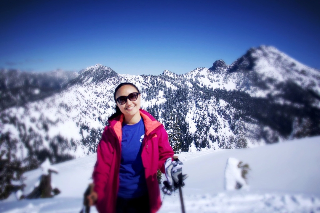 Une personne en tenue d'hiver pose devant une chaîne de montagnes enneigées.