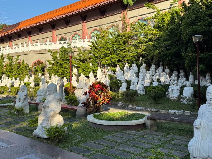 Tuin met talrijke witte stenen beelden te midden van groen.
