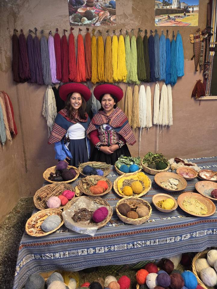 Women in traditional attire with colorful materials on a table.