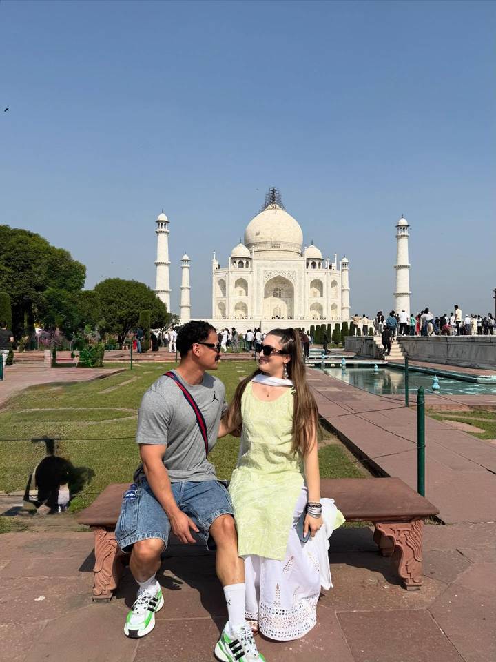 Couple souriant devant le Taj Mahal avec un ciel bleu clair.