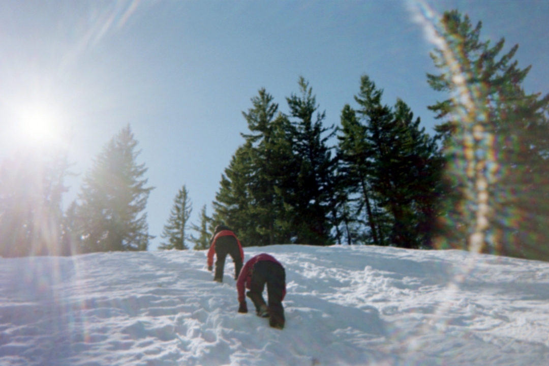 Deux personnes grimpant une colline enneigée sous un soleil radieux.