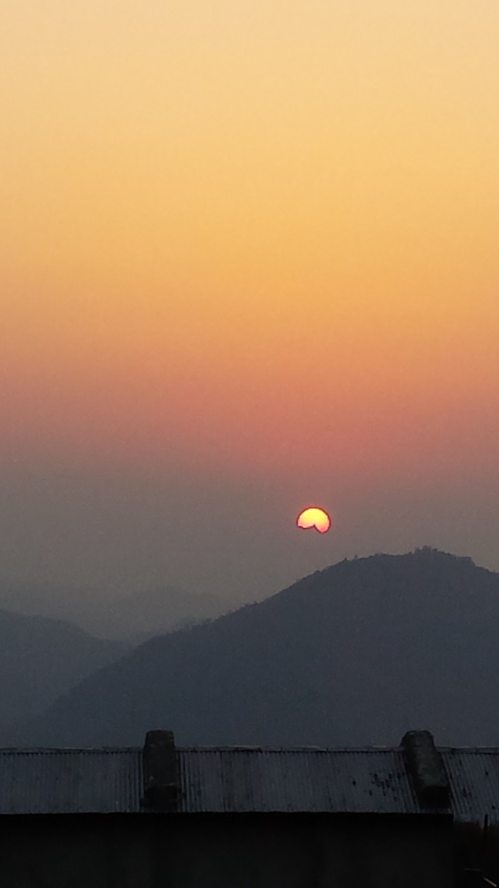 Minimalist shot of the sun half-set against hazy orange sky above a distant hill.