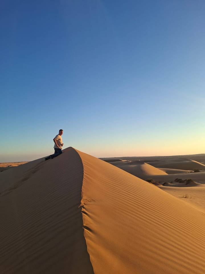 Personne au sommet d'une dune de sable dans un désert au coucher du soleil.