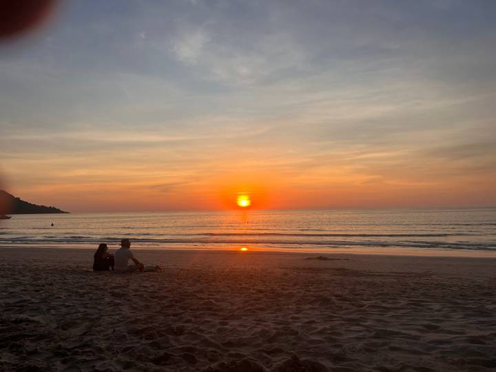 Deux personnes assises sur une plage regardant le coucher de soleil.