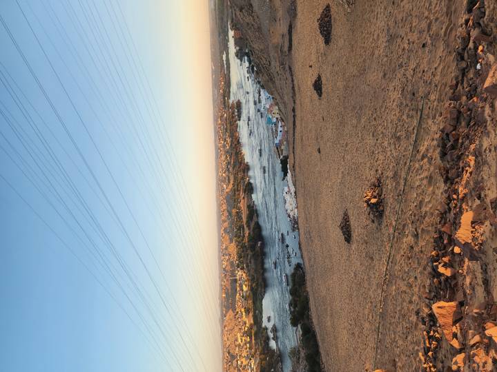 View of a river with boats, desert in the background, and power lines above.