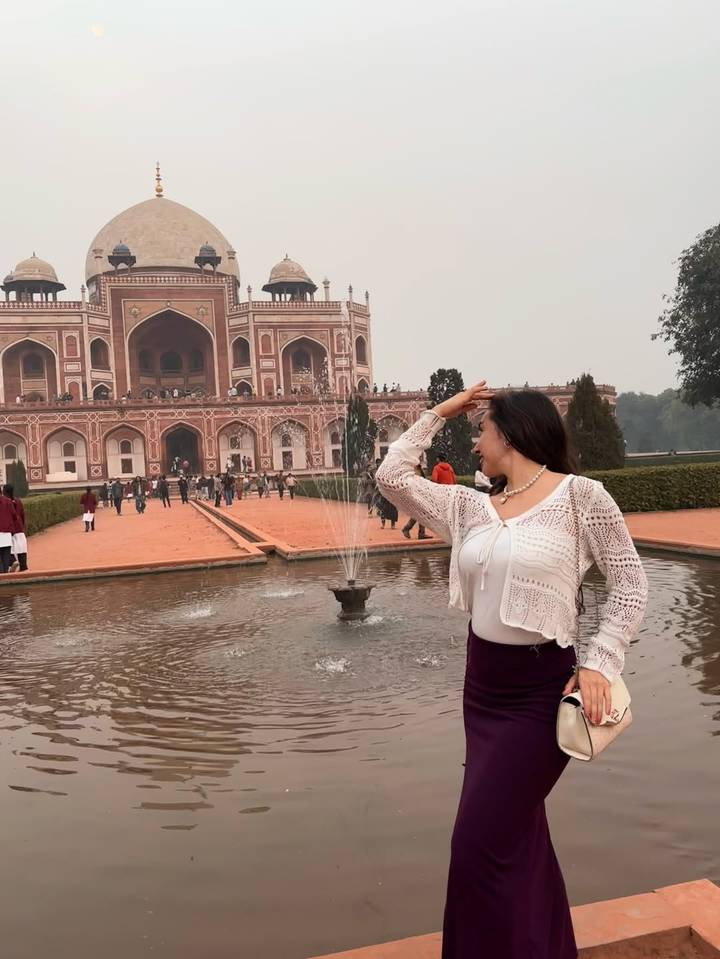 Femme posant devant une structure historique emblématique avec une fontaine.