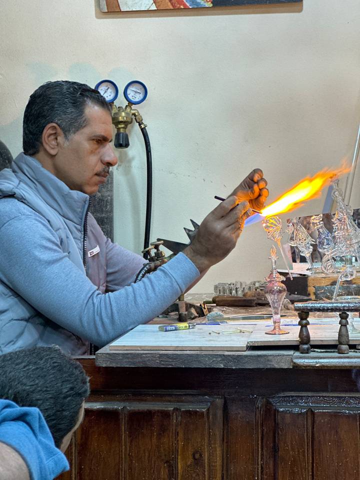 Artisan crafting glass using flame in a workshop.