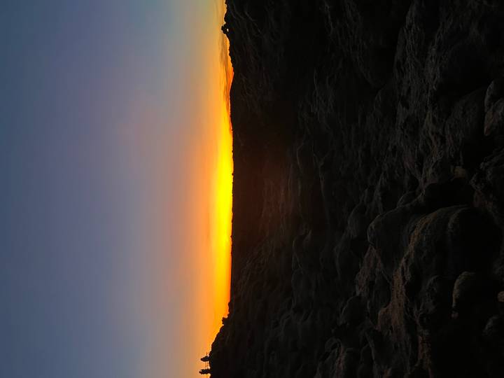 Coucher de soleil sur un terrain rocheux avec un ciel orange.