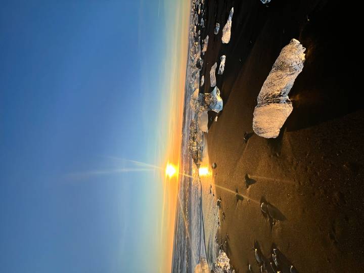 Glace sur plage de sable noir au coucher du soleil avec un soleil éclatant.