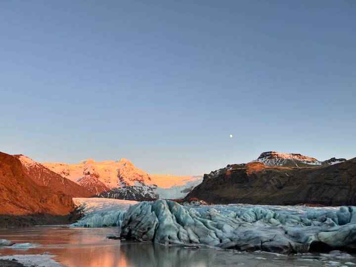 Glacier et montagnes baignés de lumière rose avec la lune au-dessus.