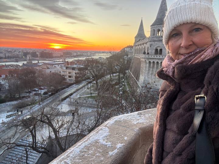 Una mujer tomándose una selfie con una vista del atardecer sobre una ciudad.