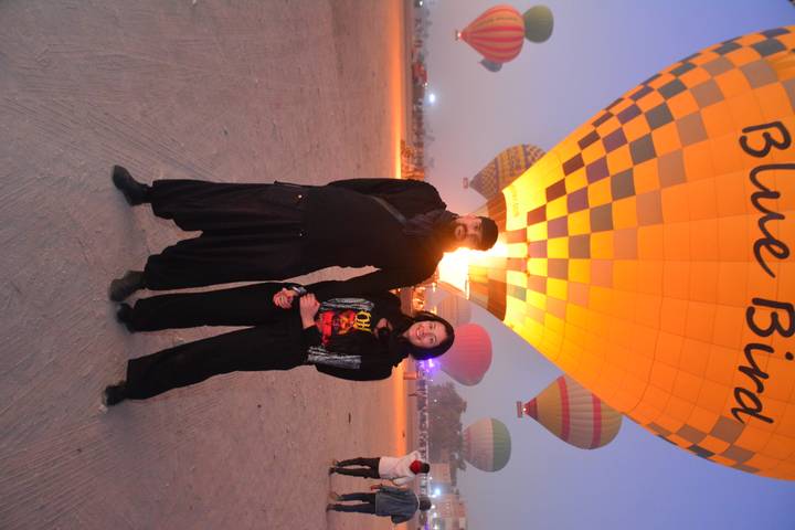 Pareja posando frente a un globo aerostático al anochecer.