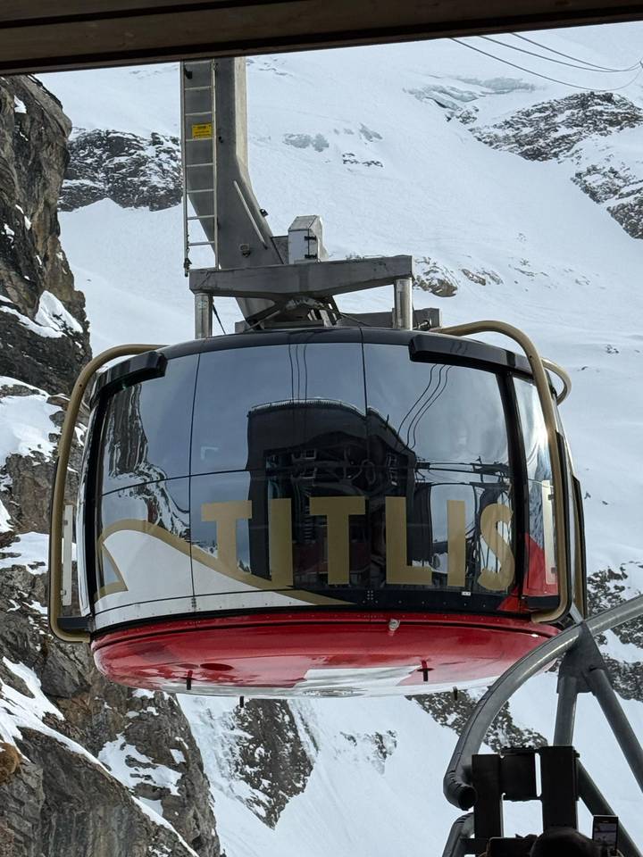 Teleférico con marca 'Titlis', fondo de montaña nevada.