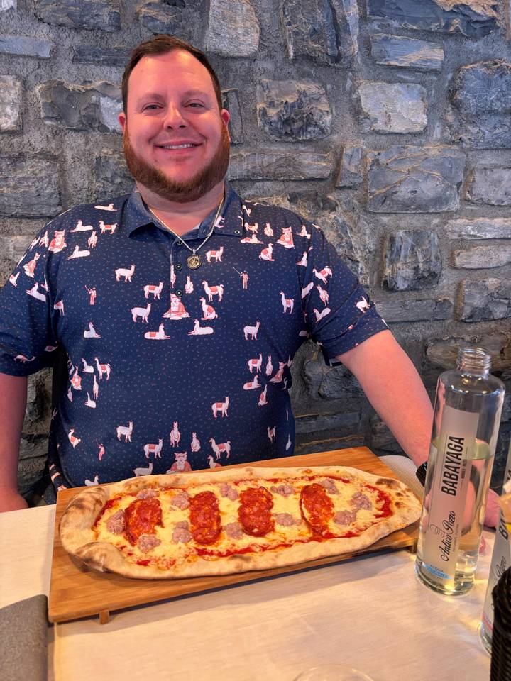 Persona con camisa temática y pizza en un lugar de mesa.