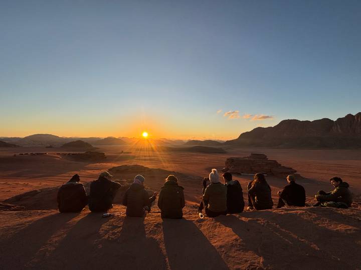 Des gens assis sur une crête regardant le coucher de soleil sur un paysage désertique.