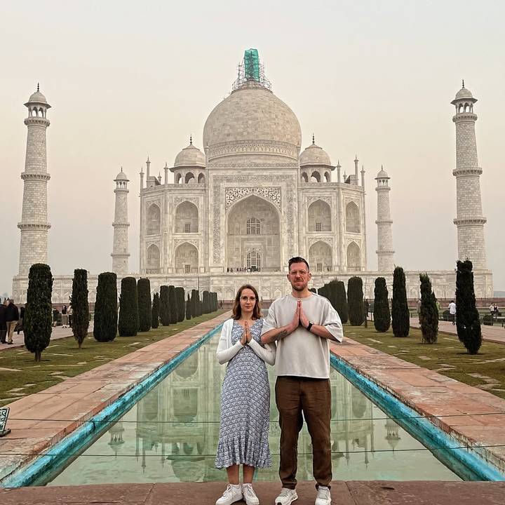 Deux touristes posant devant le Taj Mahal, les mains jointes dans un geste de namasté.
