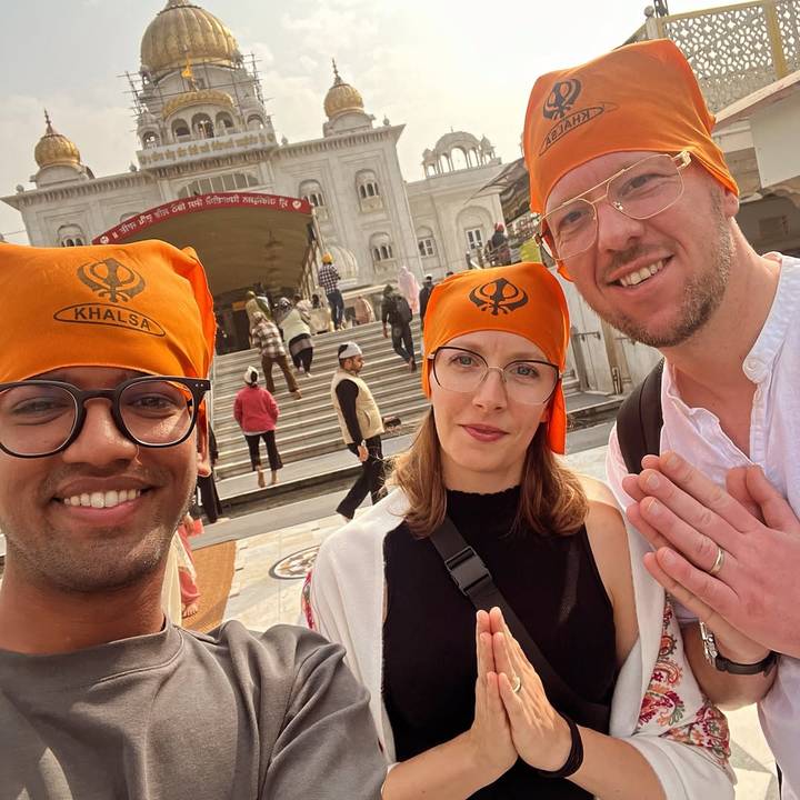 Trois personnes avec des couvre-chefs orange à l'extérieur d'un temple sikh.