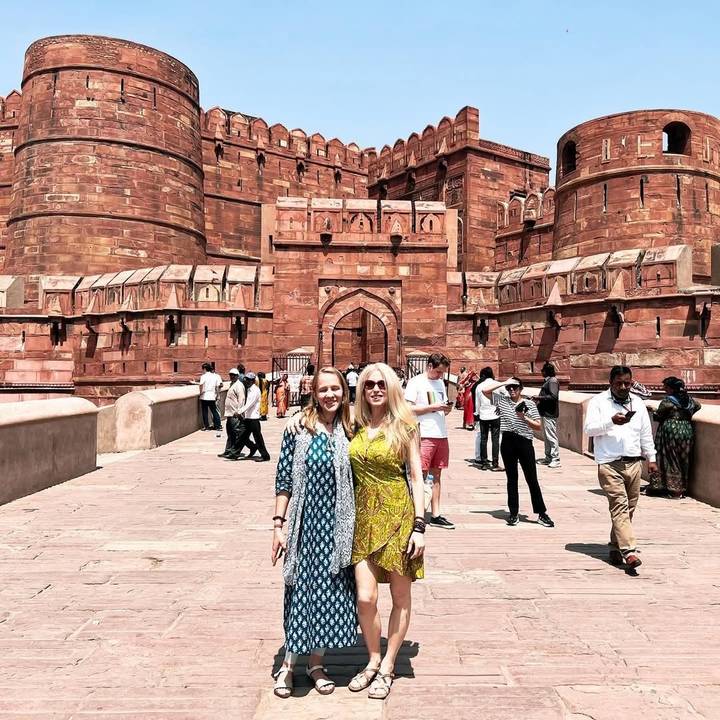 Des touristes posant devant un grand fort historique aux murs de grès rouge.