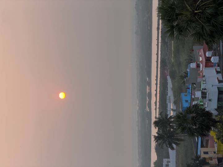 Vue lointaine du coucher de soleil sur un paysage avec des bâtiments et des palmiers.