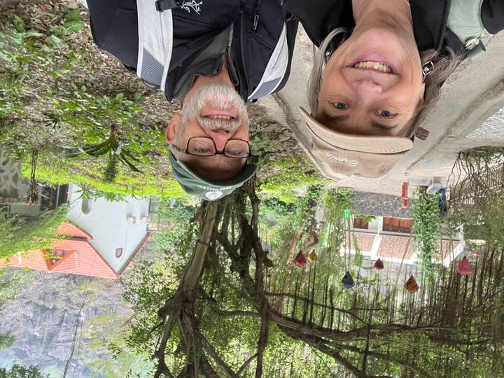 Couple prenant un selfie dans un jardin avec une architecture traditionnelle.
