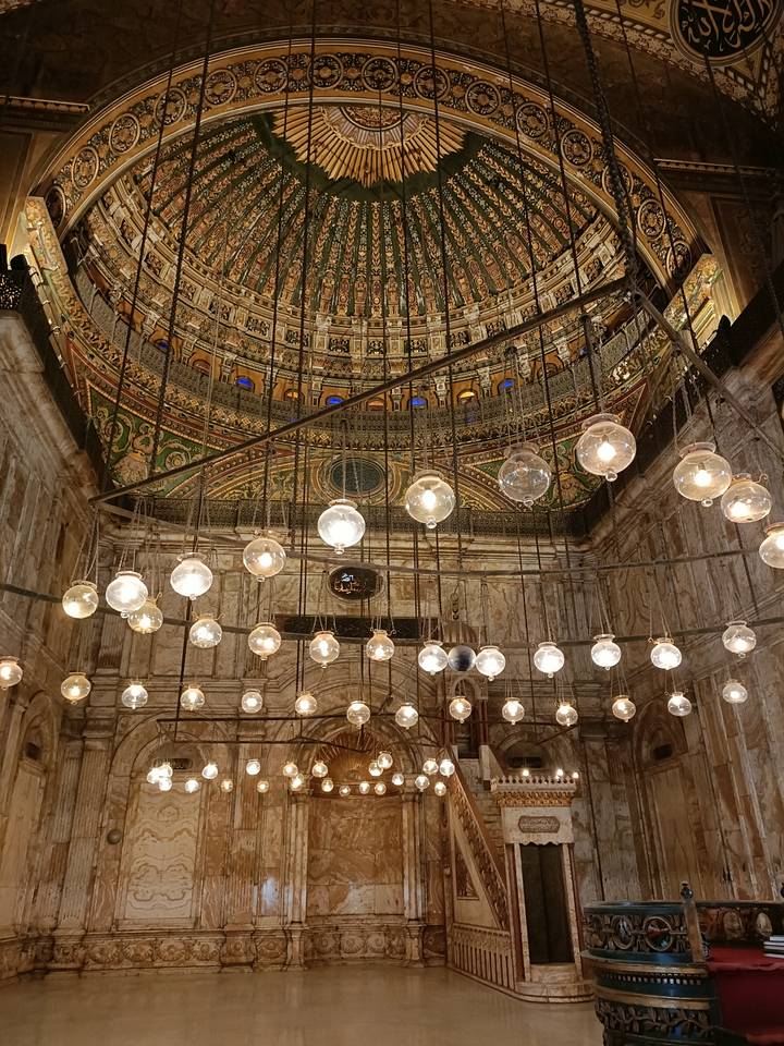 Intérieur d'une mosquée avec un plafond orné et des luminaires suspendus.