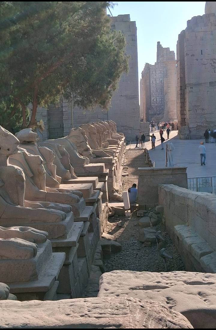 Row of stone statues leading up to an ancient temple complex.