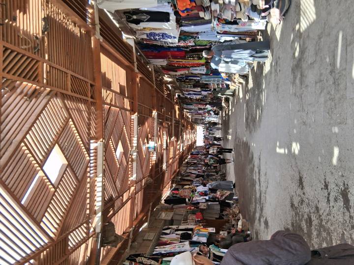 Busy market street with vendors and shoppers under wooden covering.