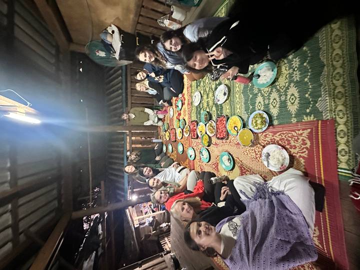 Groupe de personnes assises sur un tapis avec des plats de nourriture disposés.