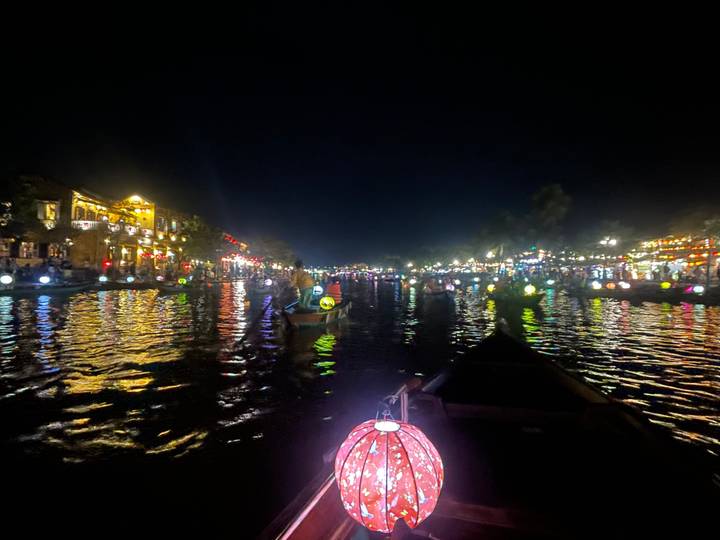 Scène de nuit sur une rivière avec des bateaux et des lumières colorées.