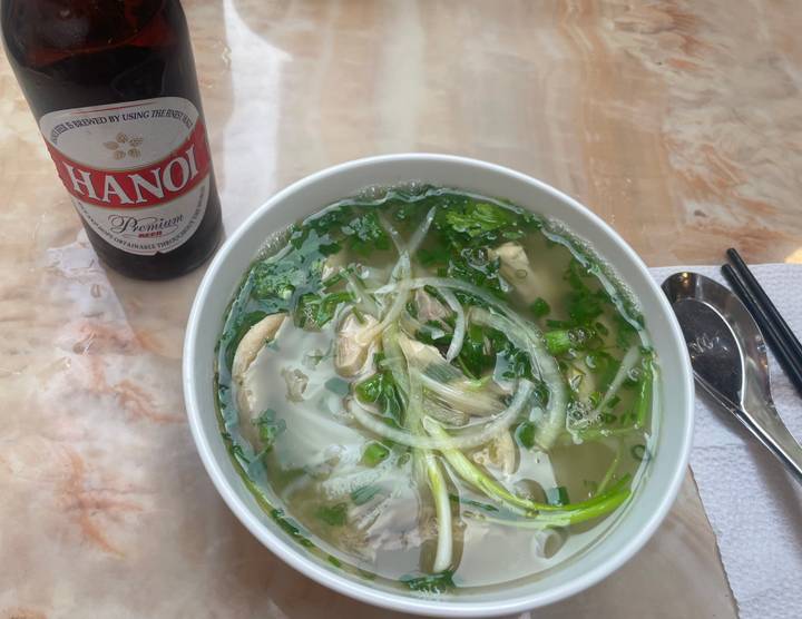 Bol de pho et une bouteille de bière Hanoi Premium sur une table.