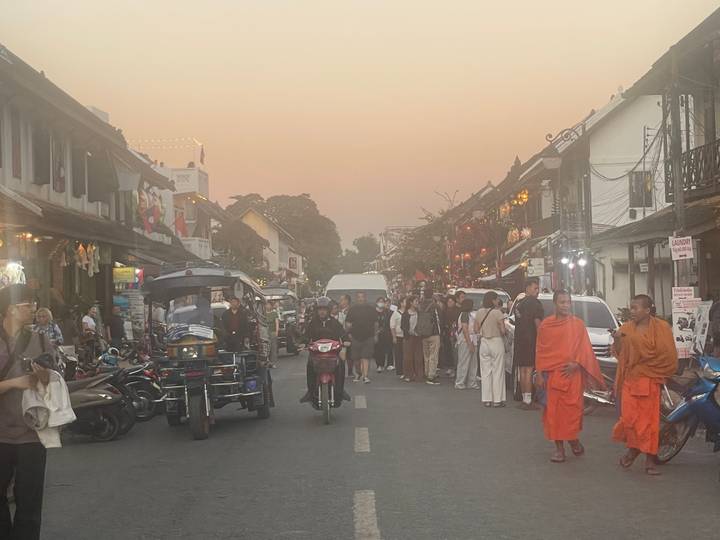 Rue animée avec des gens et des moines, sous un ciel de coucher de soleil.