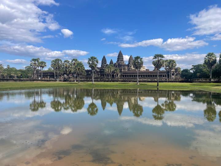 Temple d'Angkor Vat reflété dans l'eau entouré de palmiers.