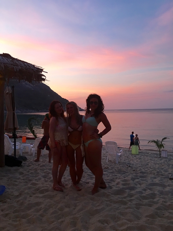 Silhouetted friends in swimwear posing on a tropical beach during a colorful sunset.