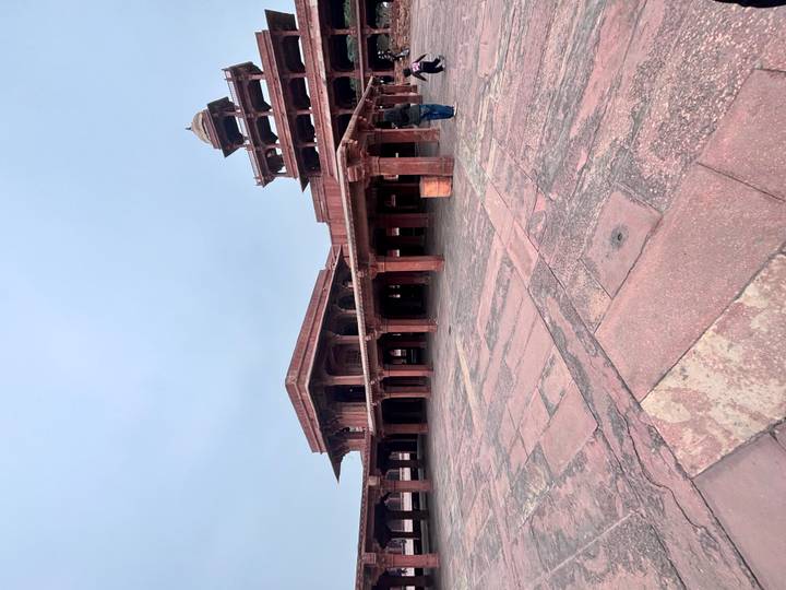 Grande cour avec des bâtiments en grès rouge et des dômes.