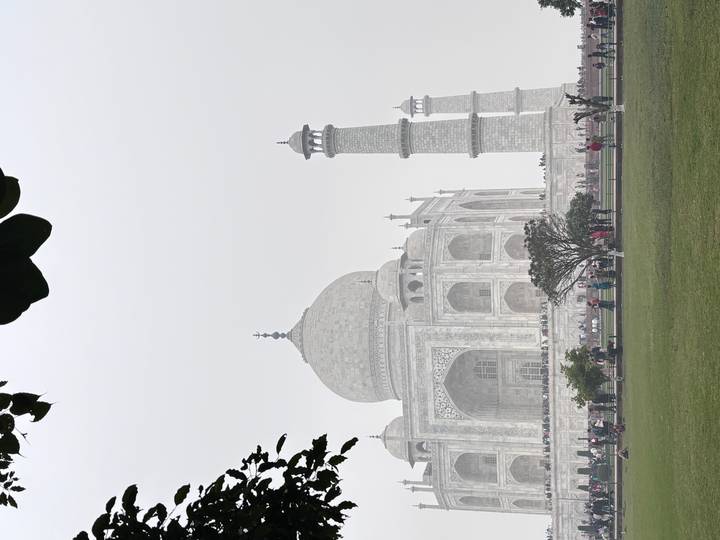 Le Taj Mahal, partiellement obscurci par le brouillard, avec des visiteurs dans le jardin.