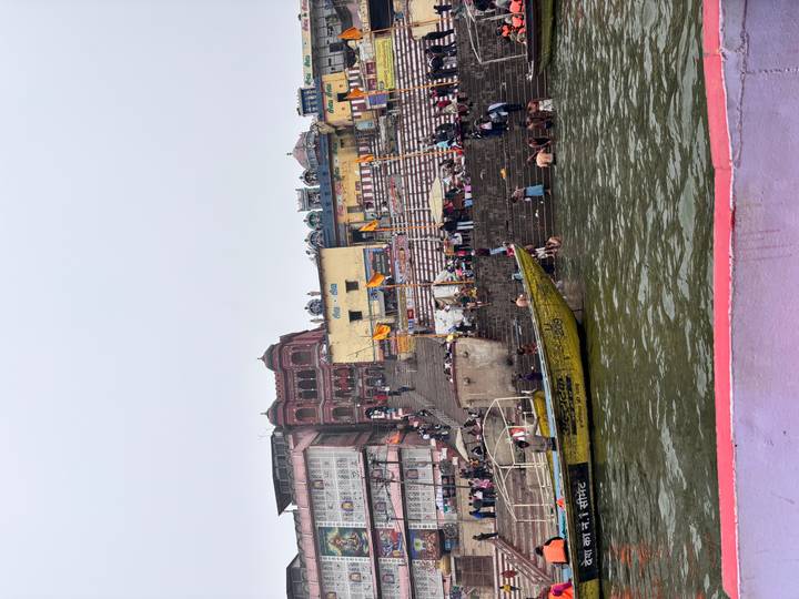 Ghat le long de la rivière avec des gens accomplissant des rituels et des bateaux à proximité.