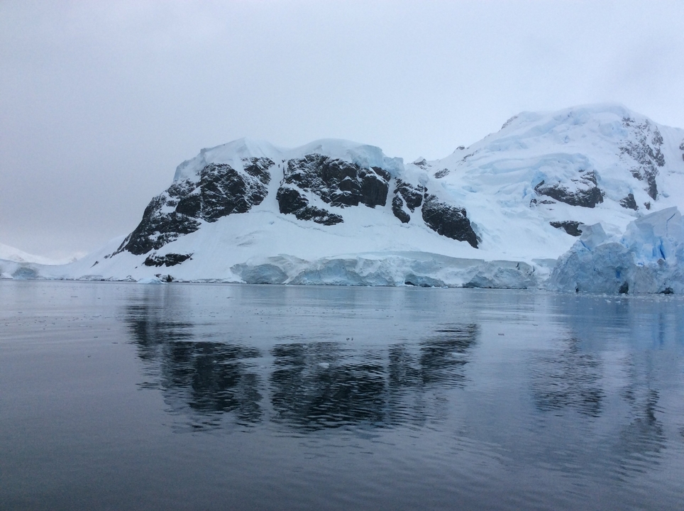 Des montagnes enneigées au bord d'une mer calme.