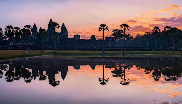 Vista del atardecer de Angkor Wat reflejado en un estanque con palmeras.